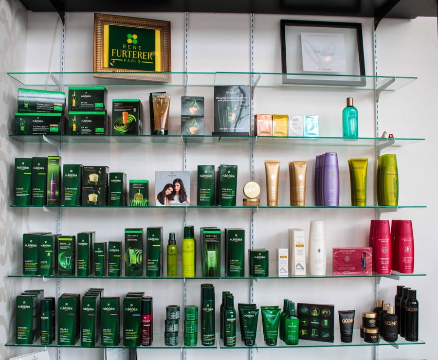 Glass shelves filled with René Furterer, Unite and Goldwell hair care, arranged by range.