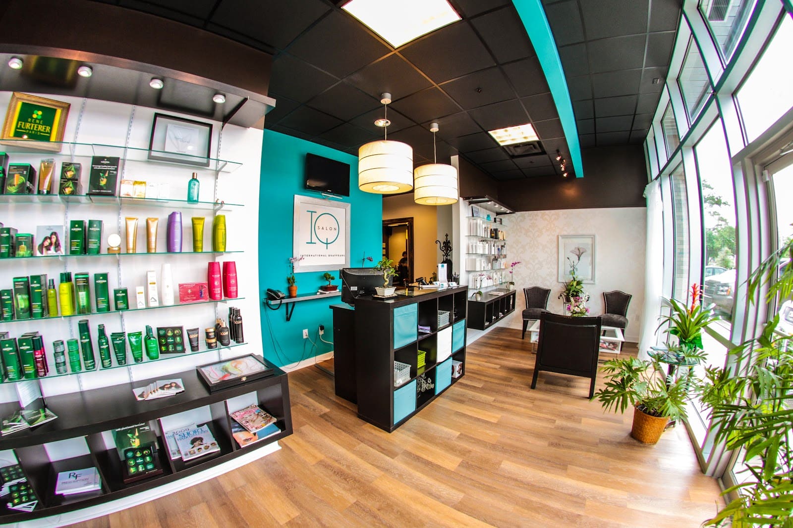The front desk against a turquoise wall under the framed IQ Salon sign, with drum pendant lights and shelves of hair products along the opposite wall.