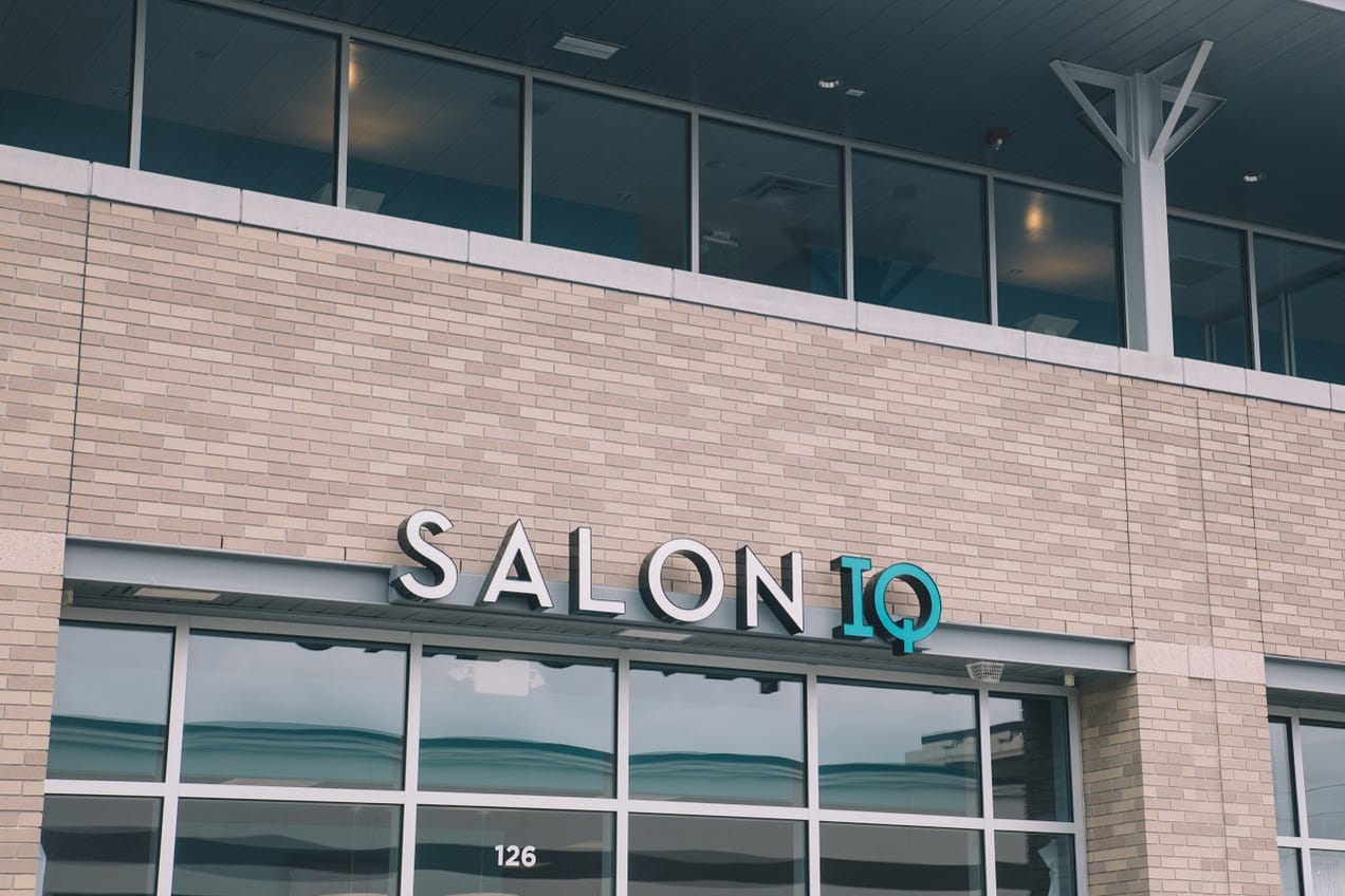 The fabricated storefront letters reading SALON in white and IQ in teal, mounted on the tan brick above the suite 126 windows.